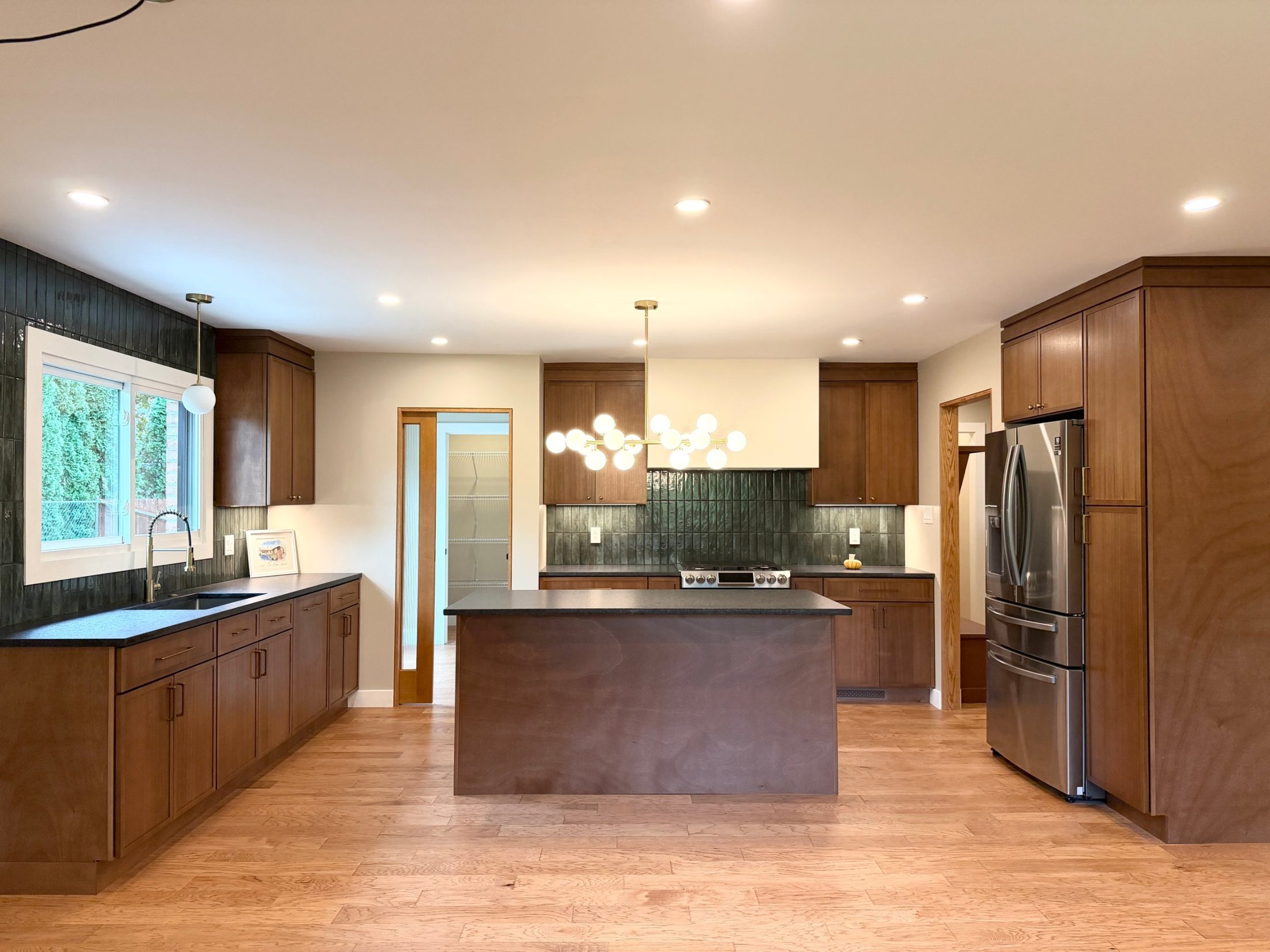 Renovated kitchen with walnut-stained cabinets, dark green tile and a center island