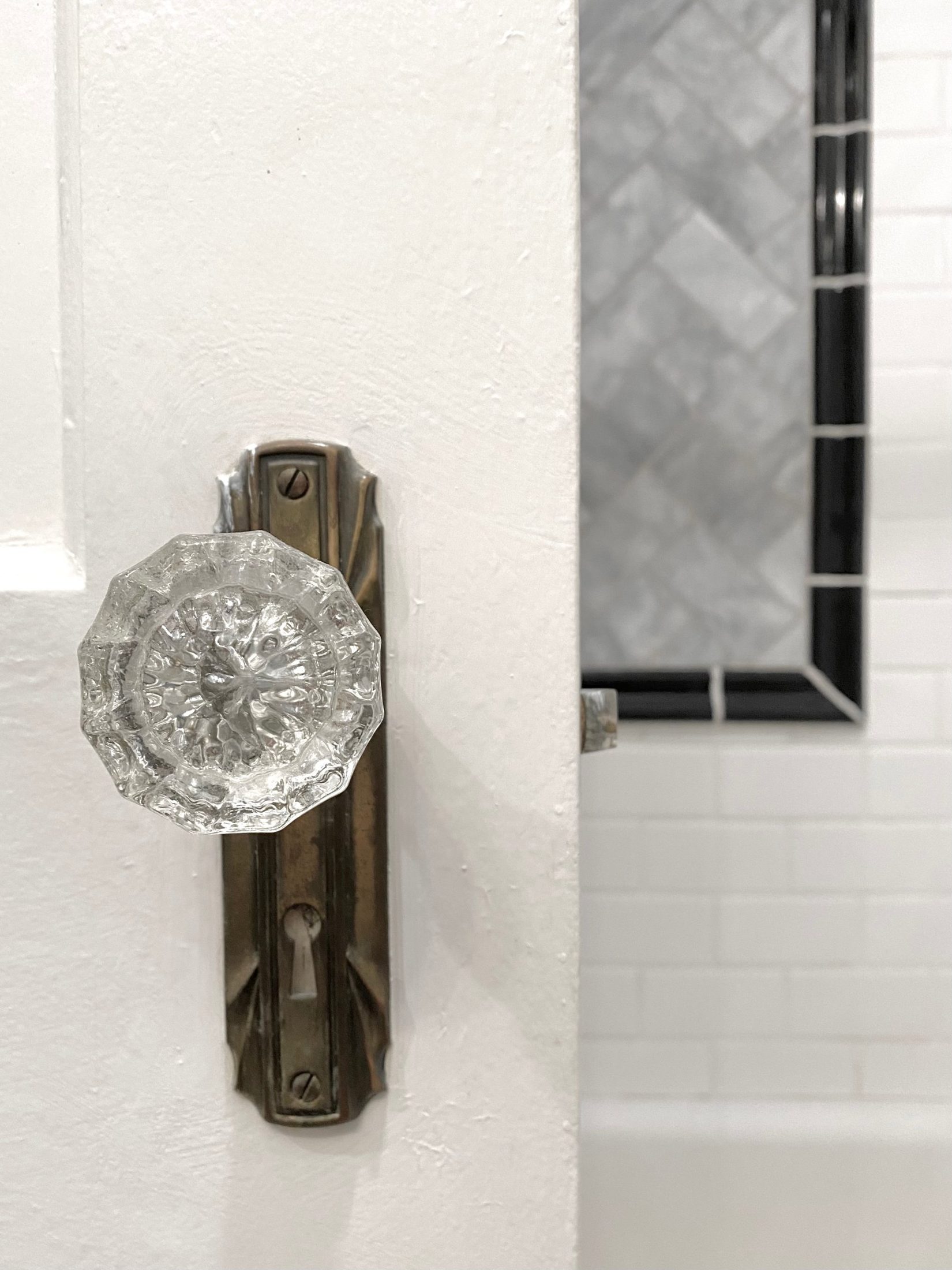 Original glass doorknob on a brass backplate beside the tiled tub wall