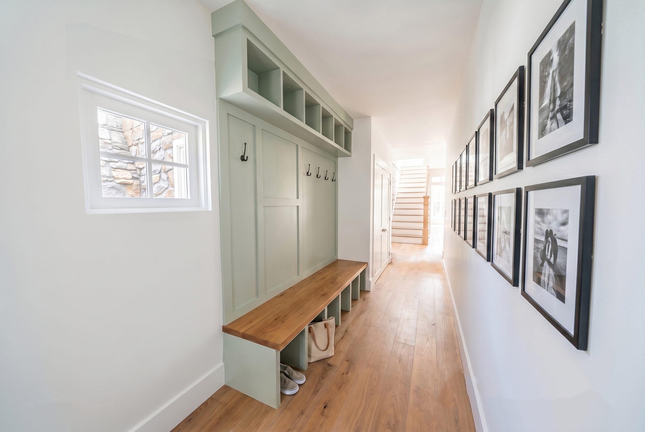 Mudroom hallway with a sage green built-in bench, cubbies and coat hooks, and a gallery wall of framed black-and-white photographs