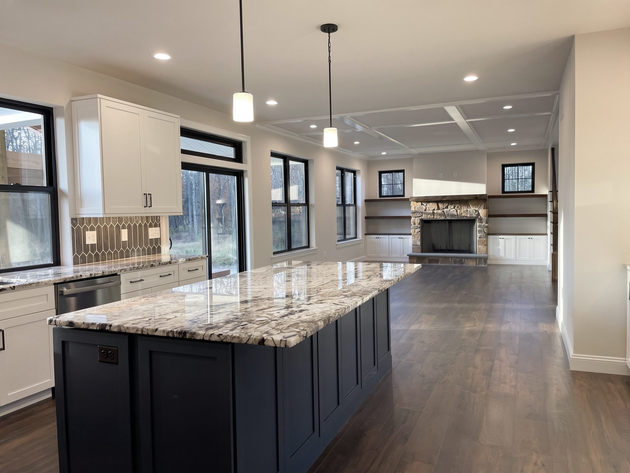 Open kitchen and living area with granite island, coffered ceiling and stone fireplace with built-in shelves