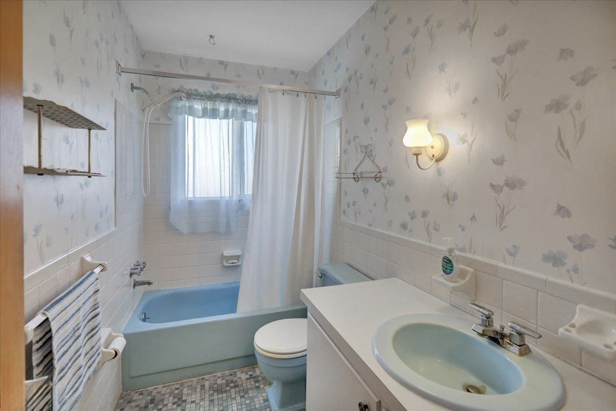 Before: the original bathroom with a blue tub, blue fixtures and floral wallpaper