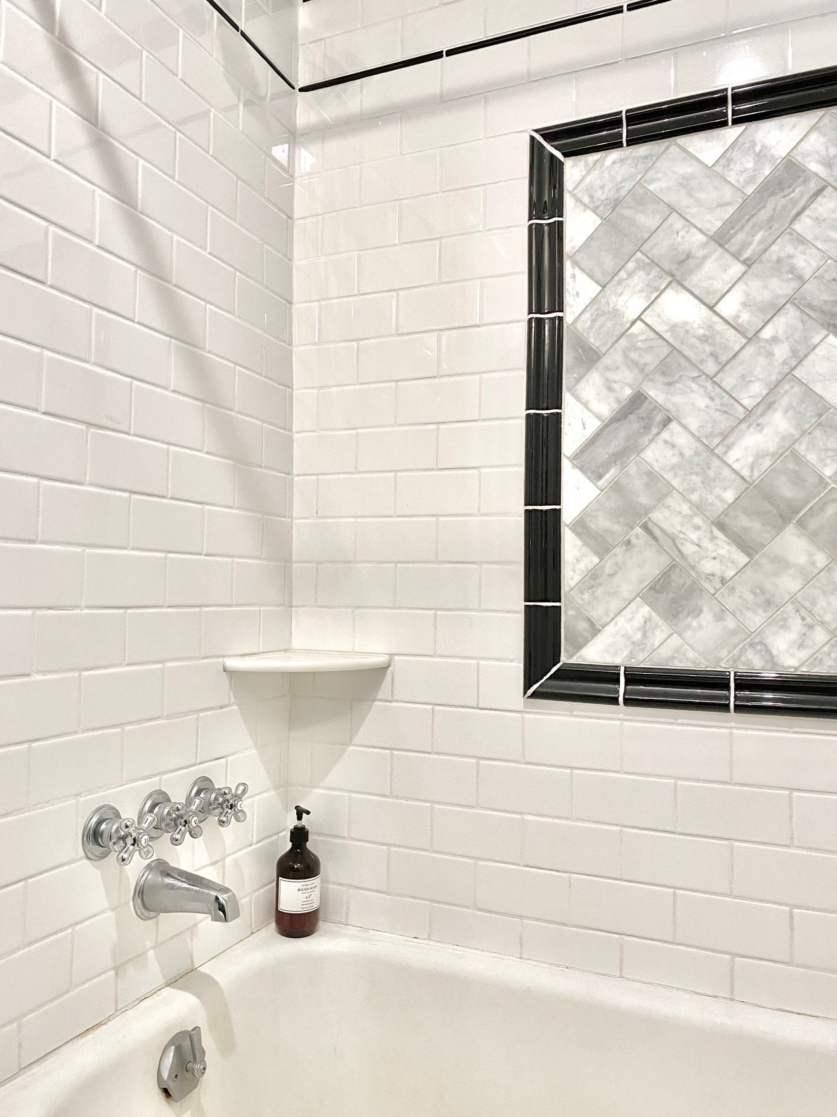 Tub surround in white subway tile with a framed marble herringbone panel